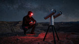 Astronomer with a red headlamp checking a phone next to the Atlas Twin at night